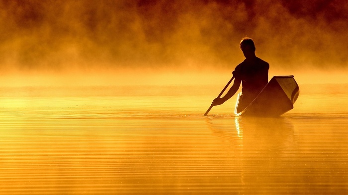 Man in a canoe paddling through misty water at sunrise