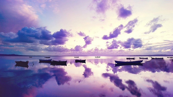 Boats on a calm lake at sunset with purple clouds