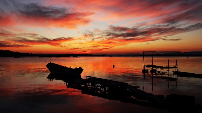 Sunset over a calm lake with a boat and pier