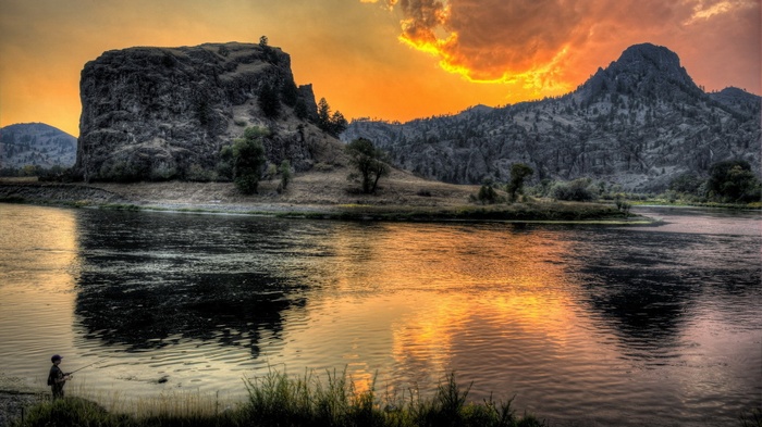 Fisherman by a river at sunset with mountains