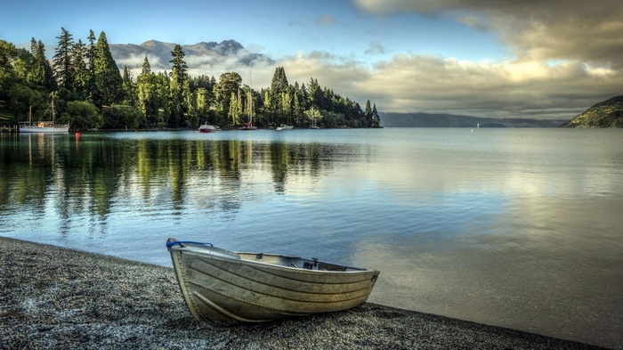 Boat on a pebble beach by a lake with trees and mountains