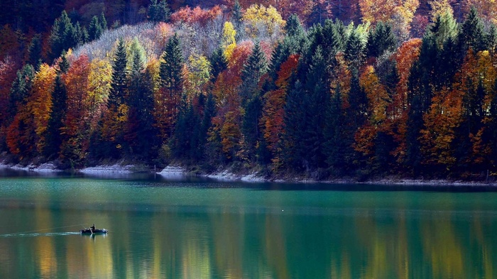 Fisherman in a boat on a lake with autumn trees