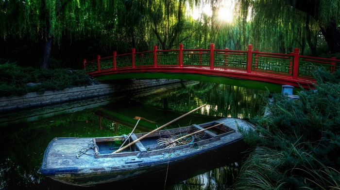 Boat under a red bridge with weeping willows
