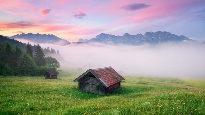 Wooden huts in a foggy mountain meadow at sunrise