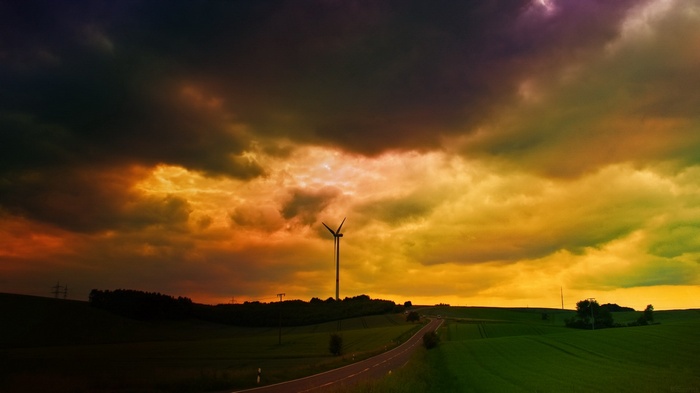 Wind turbine in a stormy, colorful sky over a rural landscape
