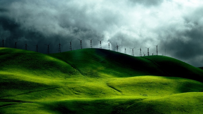 Wind turbines on green hills under stormy clouds