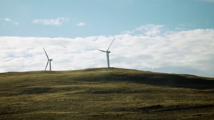 Wind turbines on a grassy hill under a cloudy sky