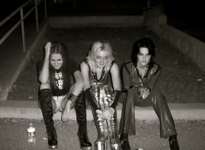 Three women in punk rock attire sitting outdoors at night