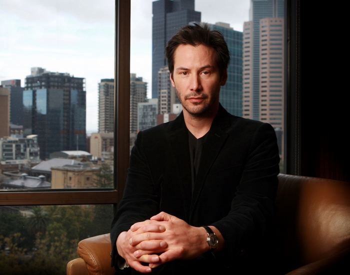 Keanu Reeves sitting in front of a city skyline