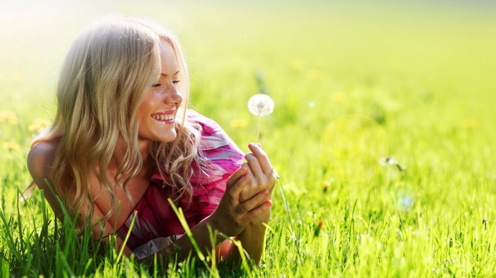 Woman lying in grass holding a dandelion