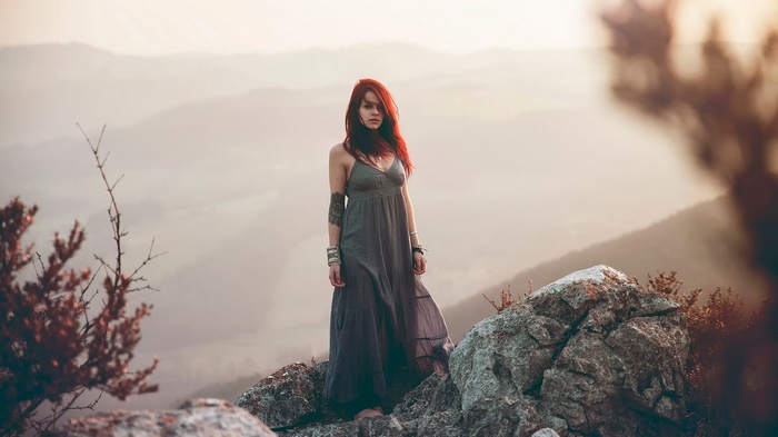 Woman with red hair in a grey dress on a rocky mountain
