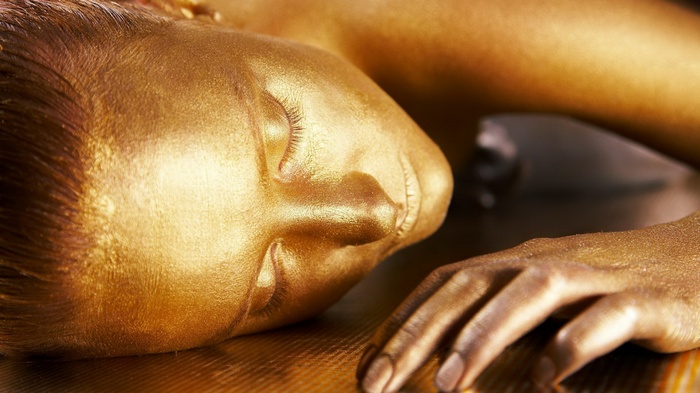 Woman covered in gold paint lying down