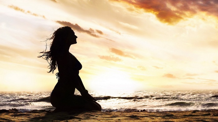 Silhouette of a woman meditating on a beach at sunset
