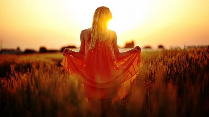 Woman in orange dress in a wheat field at sunset