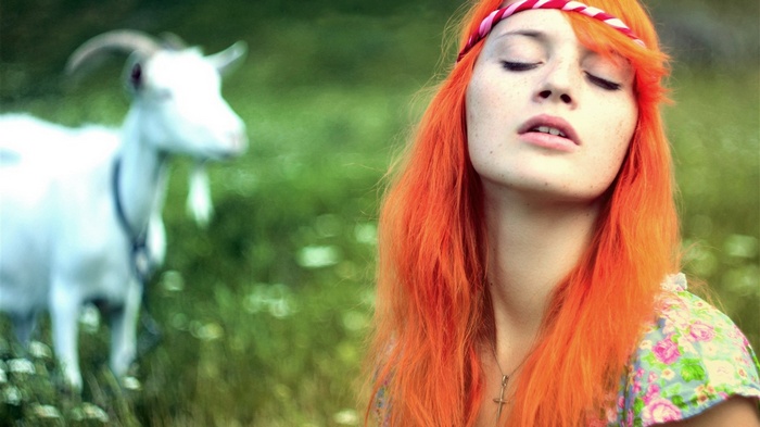 Girl with orange hair and a goat in a field