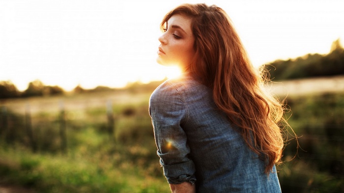 Woman with long red hair in a field at sunset