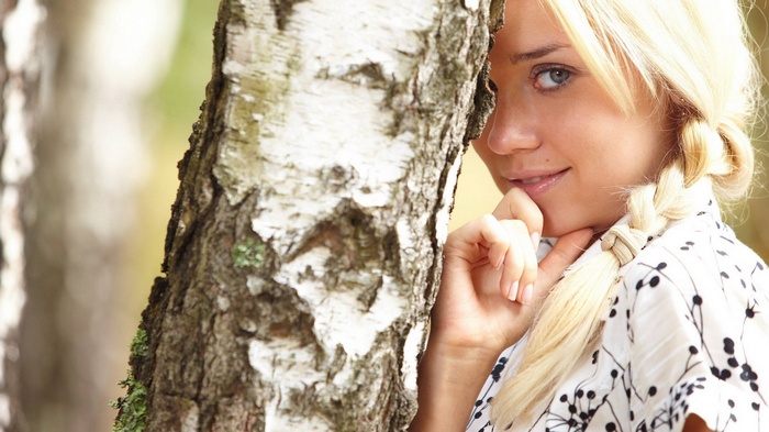 Young woman with blonde pigtails behind a birch tree
