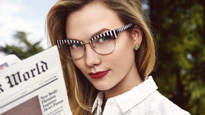 Karlie Kloss wearing striped glasses and reading a newspaper