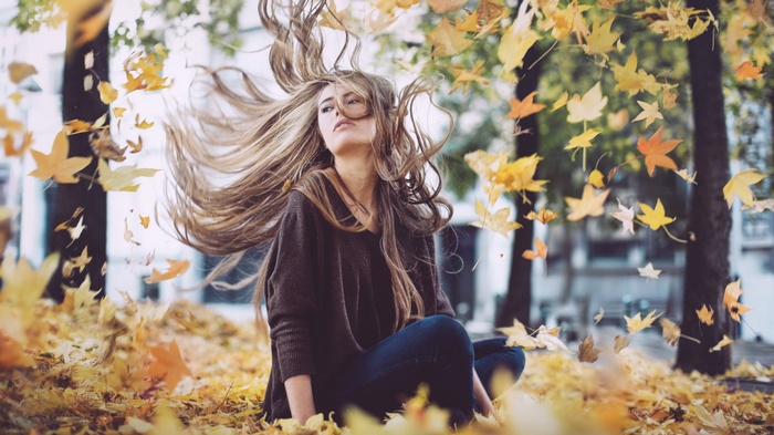Woman sitting in autumn leaves with hair blowing