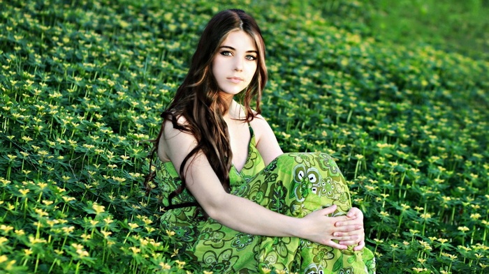 Young woman in green dress sitting in a field of flowers