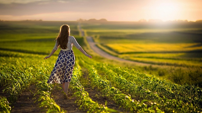 Woman walking through a field at sunset