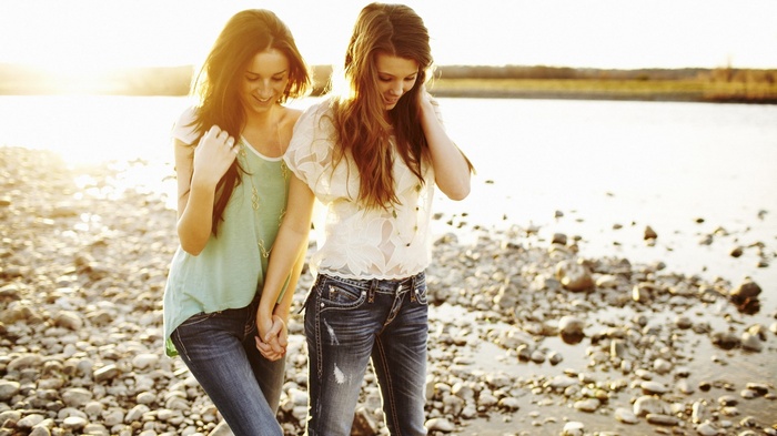 Two young women holding hands by a rocky shore
