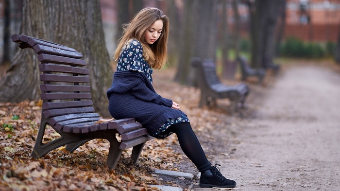 Young woman sitting alone on a park bench in autumn
