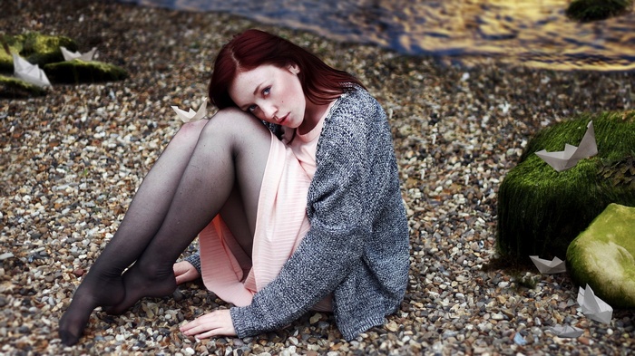 Woman sitting on a pebble beach with paper boats