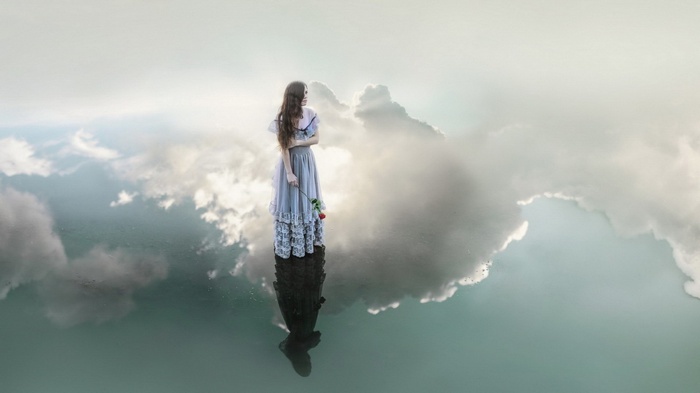 Woman in a dress holding a rose reflected in water