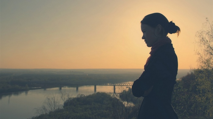 Silhouette of a woman looking over a river at sunset