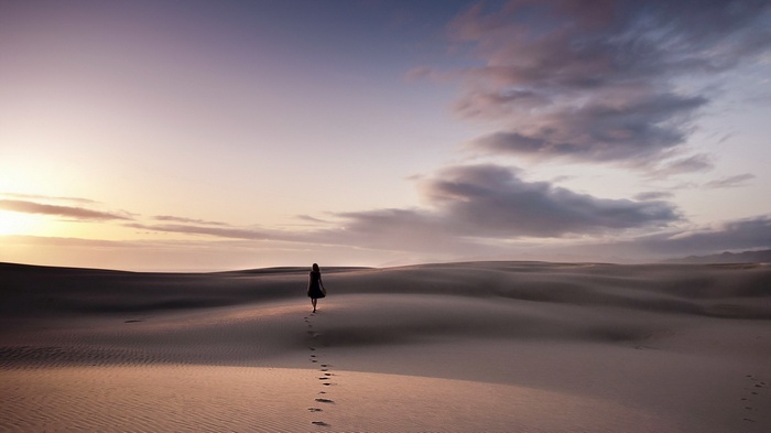 Woman walking on sand dunes at sunset