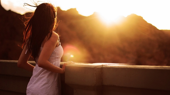 Woman in white dress looking at sunset over mountains