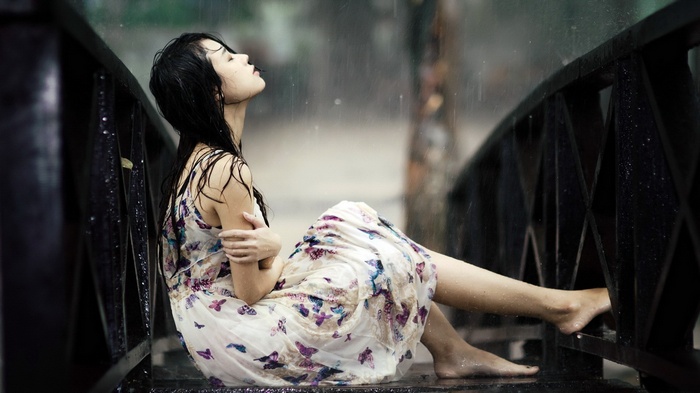 Woman in dress sitting on a bridge in the rain