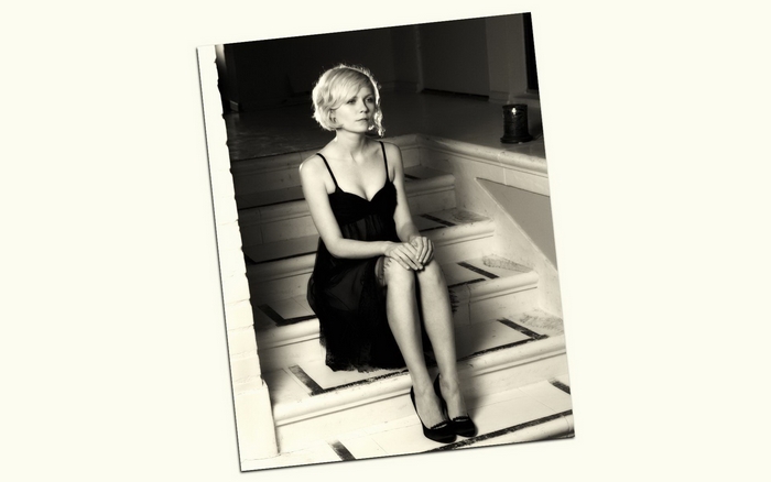 Kirsten Dunst in a black dress sitting on stairs