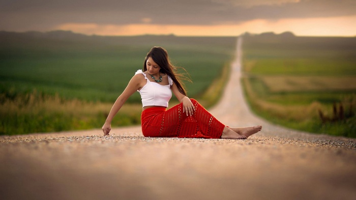 Young woman in red skirt sitting on a road