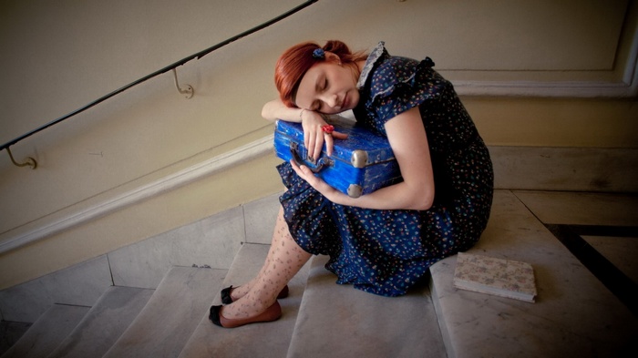 Woman sleeping on suitcase on stairs