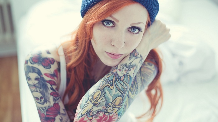 Woman with red hair and tattoos wearing a blue beanie