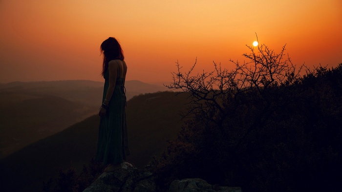 Woman in dress on cliff at sunset
