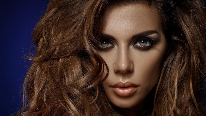 Woman with long wavy brown hair and dramatic makeup
