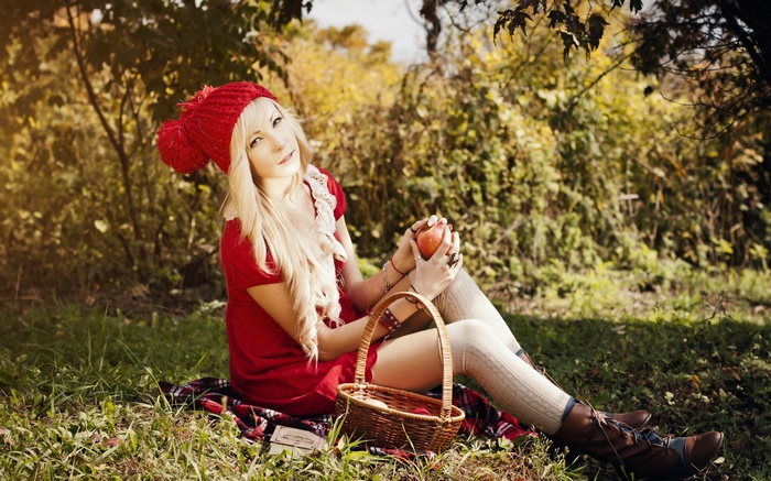 Girl in red dress and hat with apple in forest