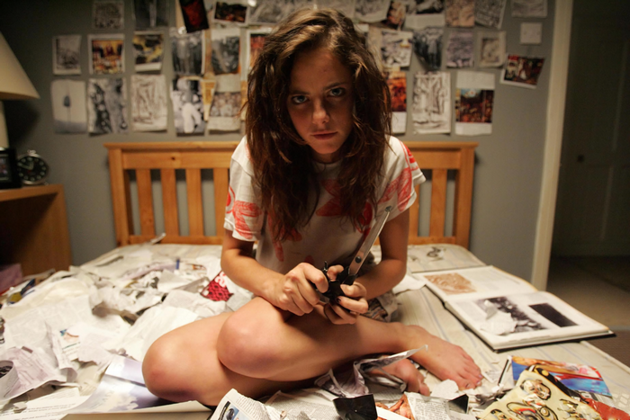 Kaya Scodelario sitting on a bed with scissors