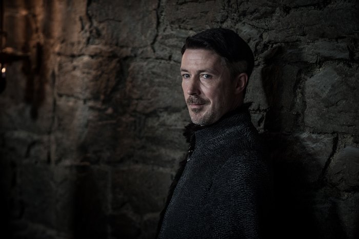 Aidan Gillen leaning against a stone wall