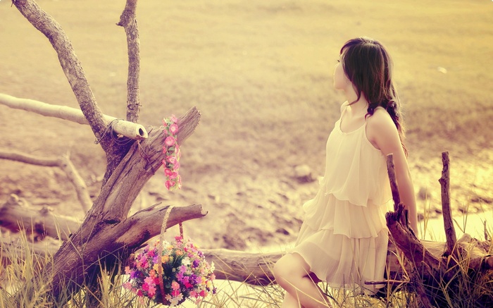 Woman in a dress sitting by a tree with flowers
