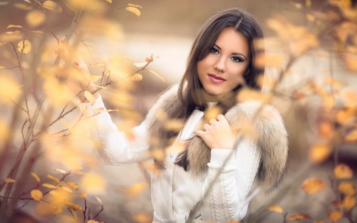 Woman in white sweater with fur collar in autumn leaves