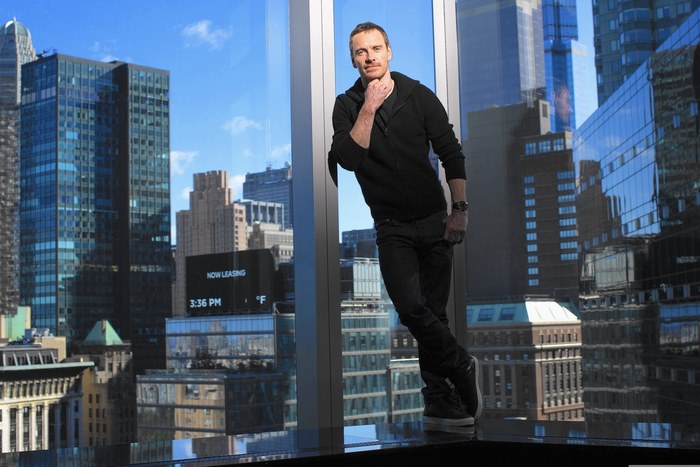 Michael Fassbender leaning by a window with city view