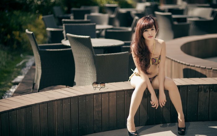 Woman in bikini sitting on a wooden bench outdoors
