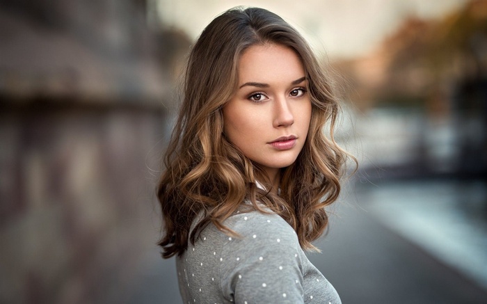 Woman with brown wavy hair wearing a grey polka dot sweater