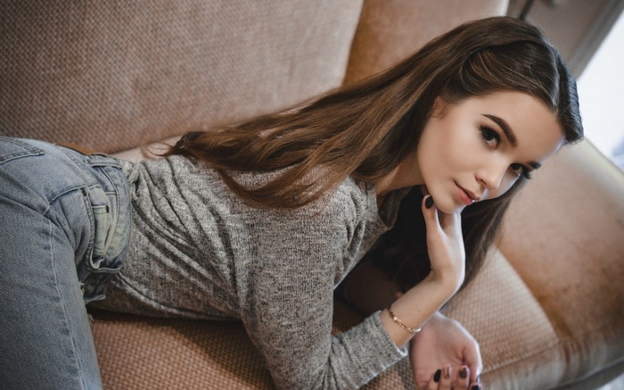 Woman in grey sweater and jeans lying on couch