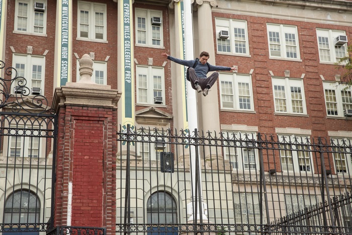 Tom Holland jumping over a fence in front of a school