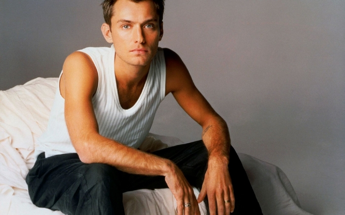 Jude Law sitting on a bed